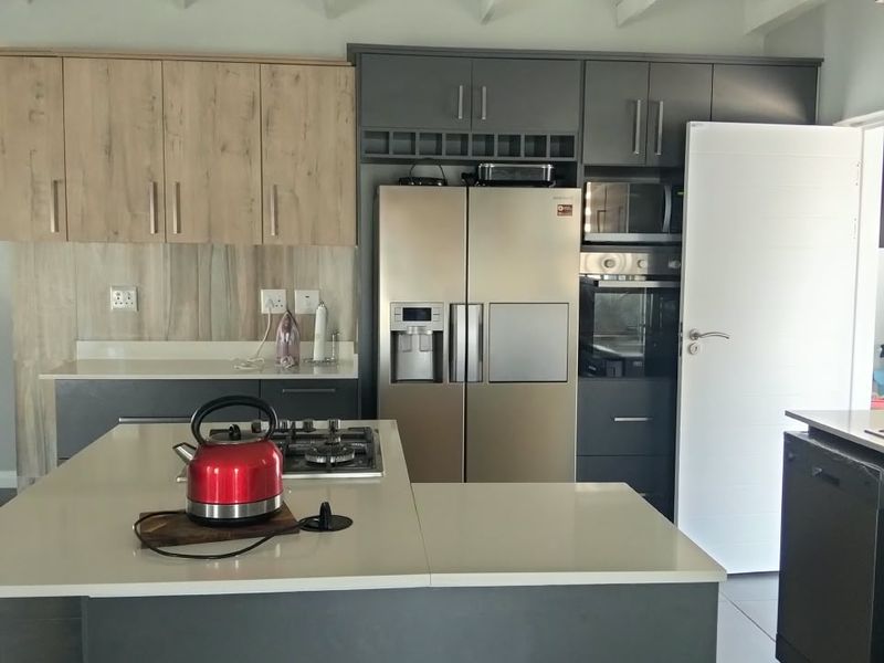 Modern kitchen featuring a central island with gas hob, stone countertops, integrated cabinetry, built-in oven, microwave, and striking exposed white roof trusses.