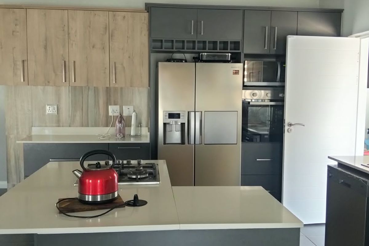 Modern kitchen featuring a central island with gas hob, stone countertops, integrated cabinetry, built-in oven, microwave, and striking exposed white roof trusses.