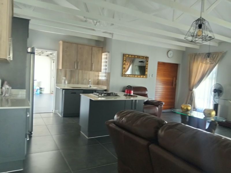 Open-plan living area featuring a modern kitchen with a central island, gas hob, tiled flooring, and exposed beam ceilings, flowing into the lounge space.