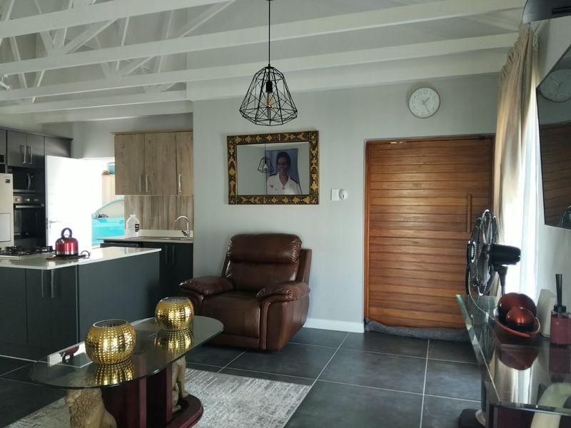 Open-plan living area featuring exposed white rafters, tiled flooring, and a modern kitchen with built-in cabinetry and a central island.