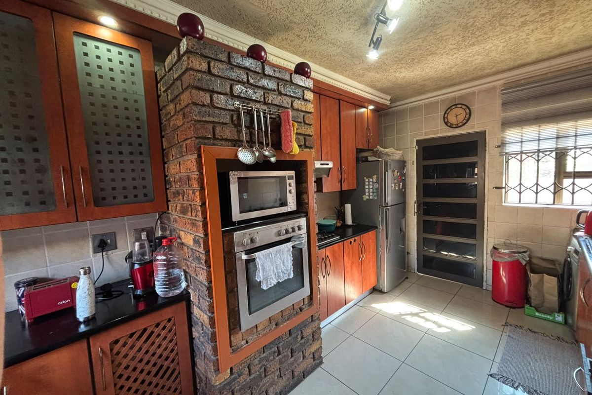 A functional kitchen featuring wooden cabinetry, a unique brick feature pillar housing the oven and microwave, tiled flooring, and a security door.