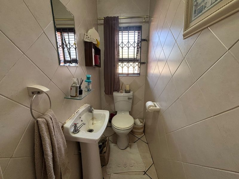 A compact guest bathroom featuring a pedestal basin, toilet, and full-height tiled walls with a security gate on the window.