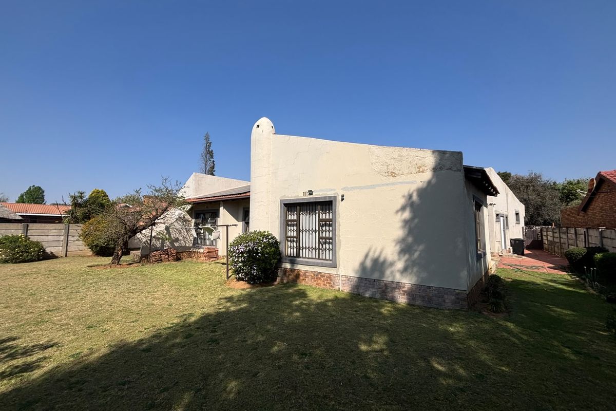 Rear view of the house showing the garden, exterior walls with visible plaster damage, security bars on windows, and perimeter boundary wall.