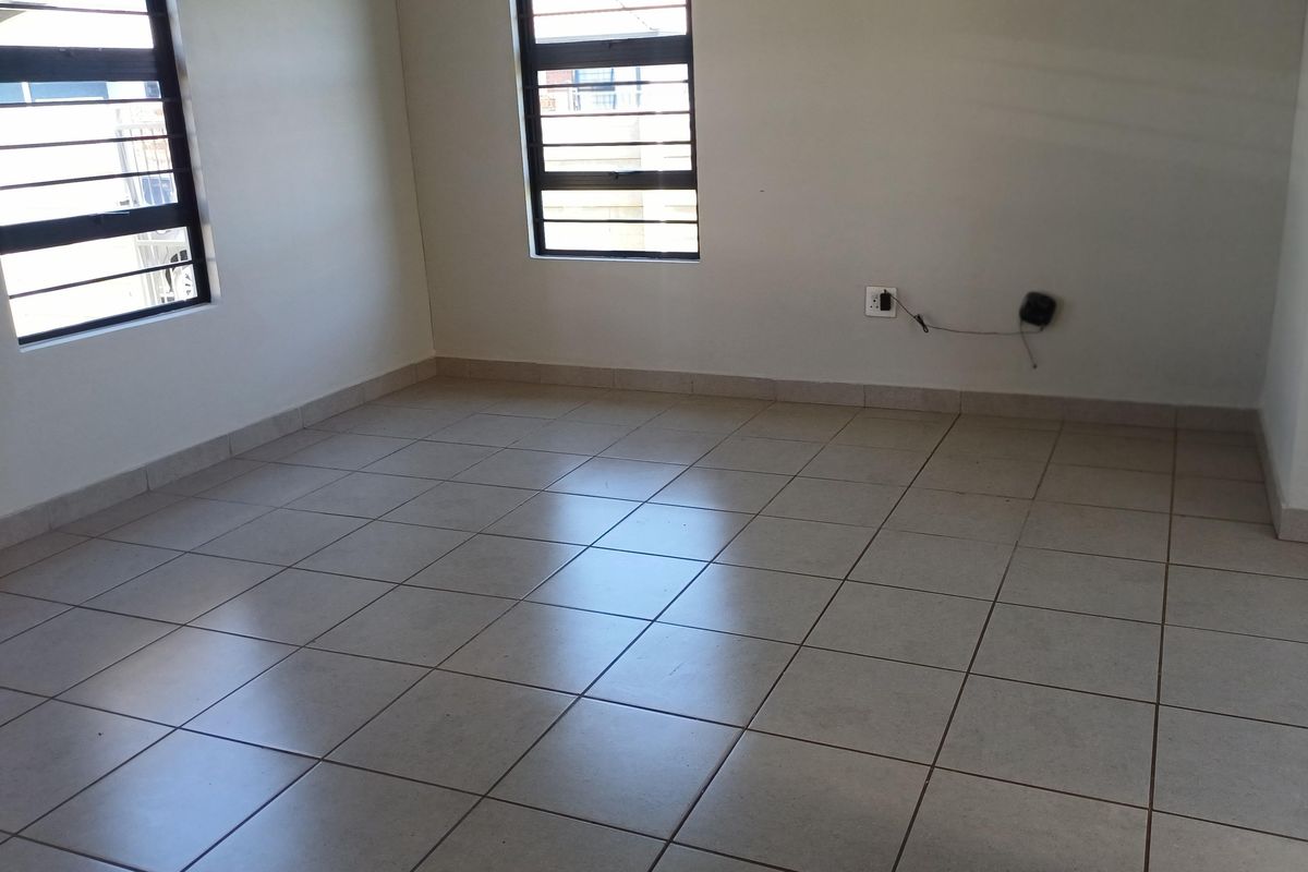 An empty living area featuring neutral tiled flooring and windows fitted with security bars, providing a clean and versatile space.