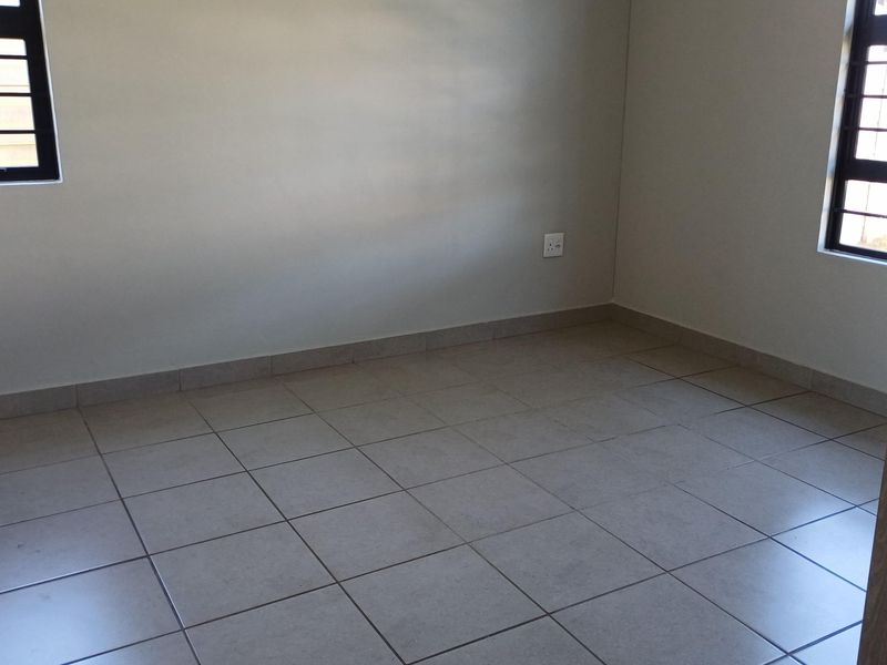 A clean, empty bedroom featuring neutral tiled flooring, security bars on the windows, and simple finishes, ready for personalization.