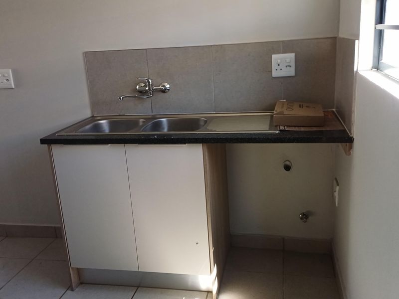A functional laundry area featuring a double stainless steel sink, tiled splashback, and dedicated plumbing connections for a washing machine.