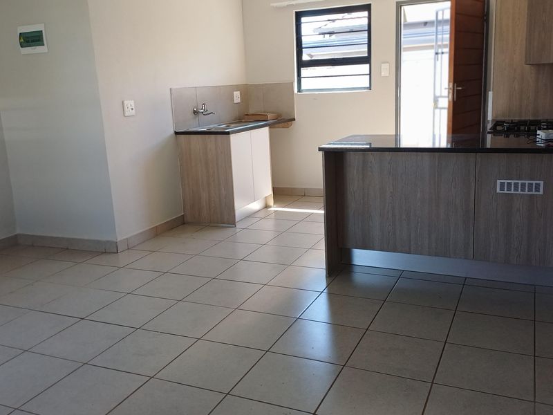 An open-plan kitchen area featuring modern wood-look cabinetry, granite countertops, a built-in gas hob, and neutral tiled flooring throughout.