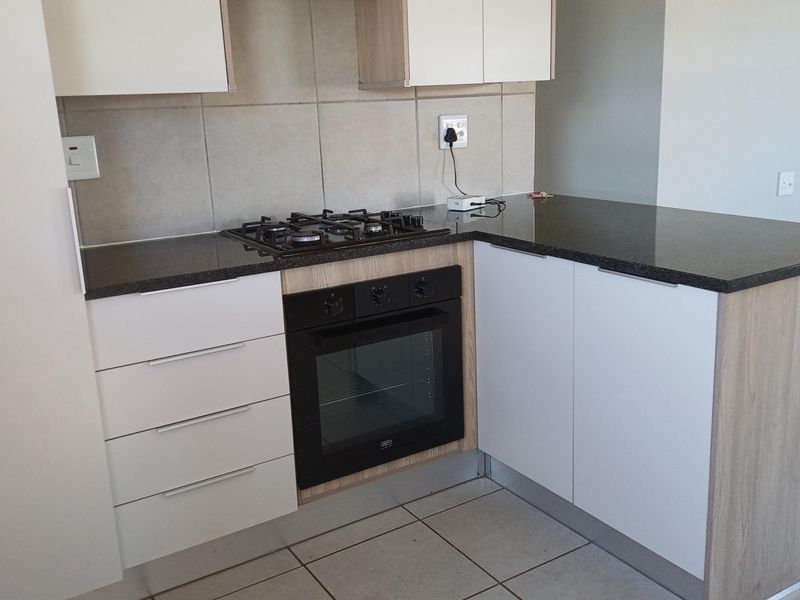 Modern kitchen featuring sleek white and wood-tone cabinetry, dark granite countertops, a built-in oven, and a gas hob with tiled splashback.