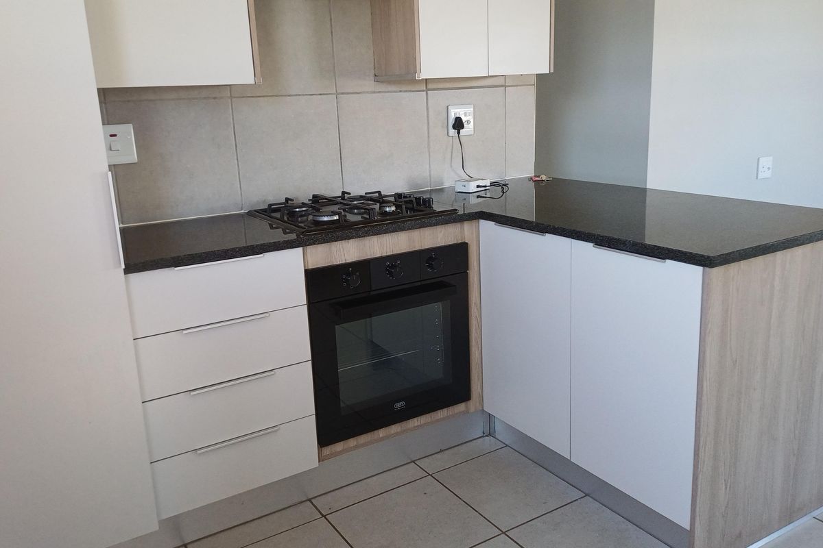 Modern kitchen featuring sleek white and wood-tone cabinetry, dark granite countertops, a built-in oven, and a gas hob with tiled splashback.