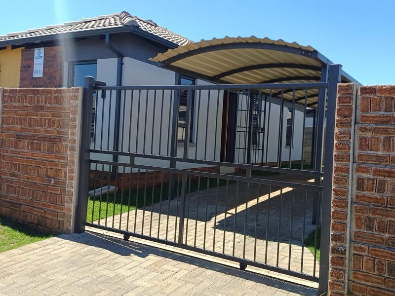 Front view of the property featuring a secure metal gate, paved driveway, and a covered carport area.