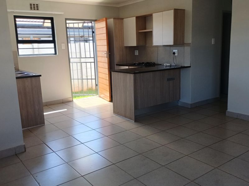 Open-plan kitchen and living area featuring tiled floors, modern cabinetry with granite countertops, and direct access to the exterior via a security gate.
