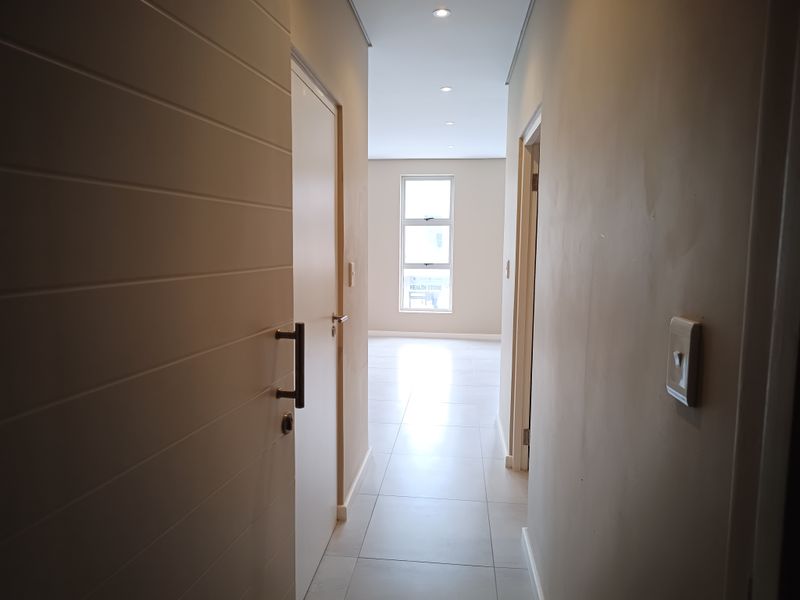 A bright, modern hallway featuring neutral tiled flooring, recessed downlighting, and clean interior doors leading to adjacent rooms.
