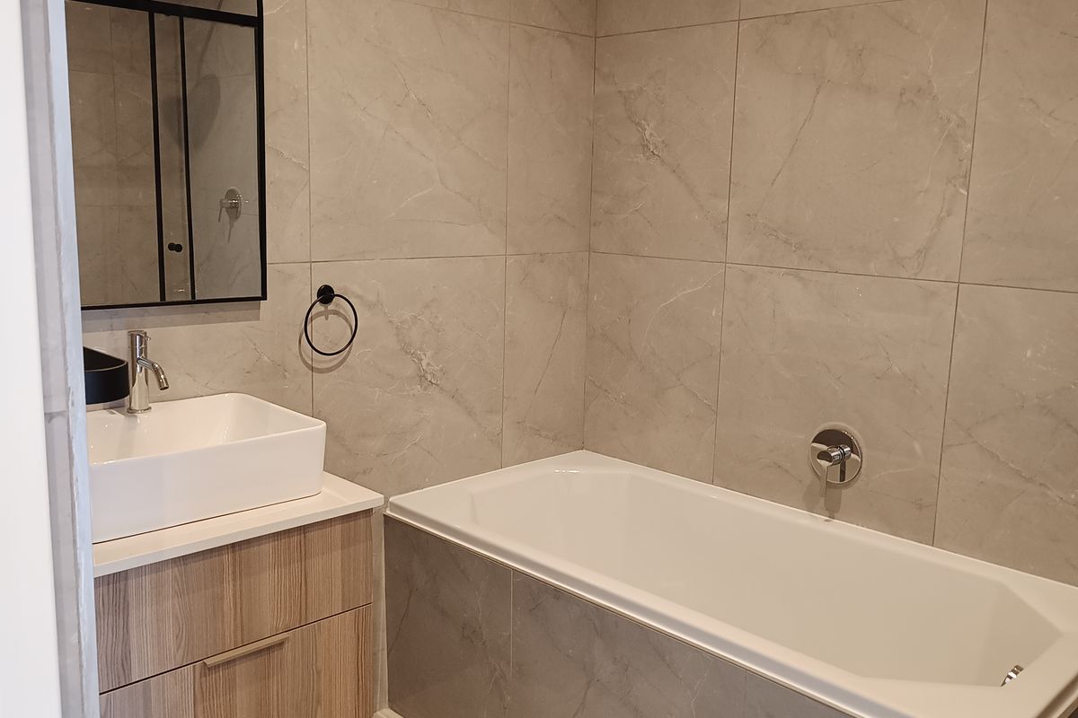 Modern bathroom featuring a wall-mounted vanity, vessel sink, built-in bathtub, and elegant large-format tiled walls and flooring.