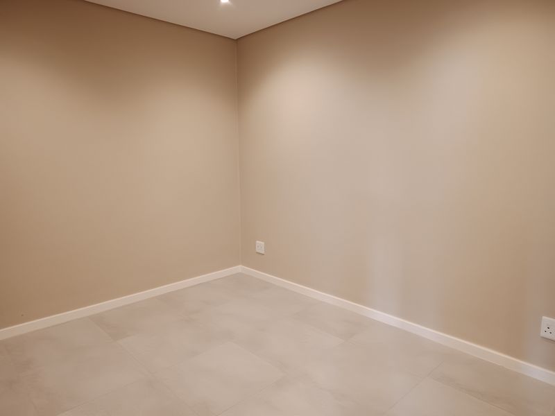 A clean, empty bedroom featuring neutral painted walls, modern tiled flooring, and recessed ceiling lighting.