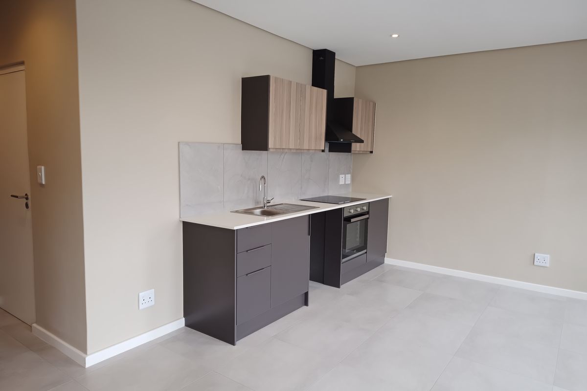 Modern, compact kitchen featuring sleek dark cabinetry, stone countertops, integrated oven, hob, and extractor fan, set against a neutral tiled floor.
