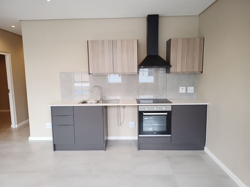 Modern kitchen featuring sleek grey and wood-tone cabinetry, integrated electric oven and hob, extractor fan, and a clean stone-look splashback.