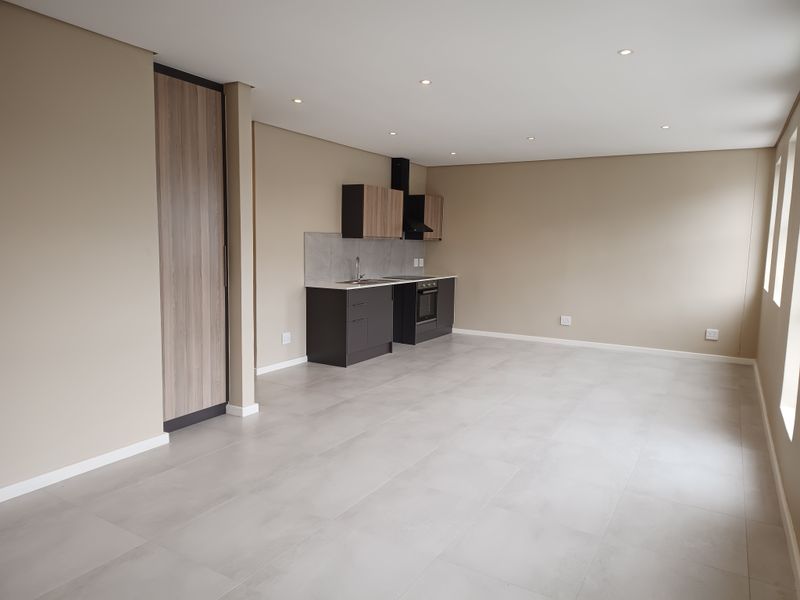 Modern open-plan living area featuring a sleek kitchen with built-in cabinetry, integrated oven, extractor fan, and neutral tiled flooring throughout.
