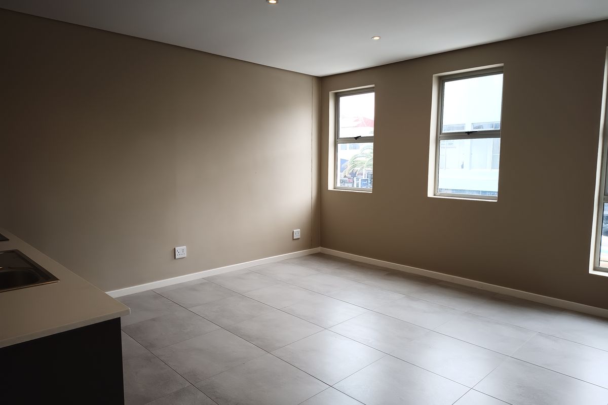 An empty open-plan living and kitchen area featuring modern tiled flooring, recessed downlights, and neutral wall tones.