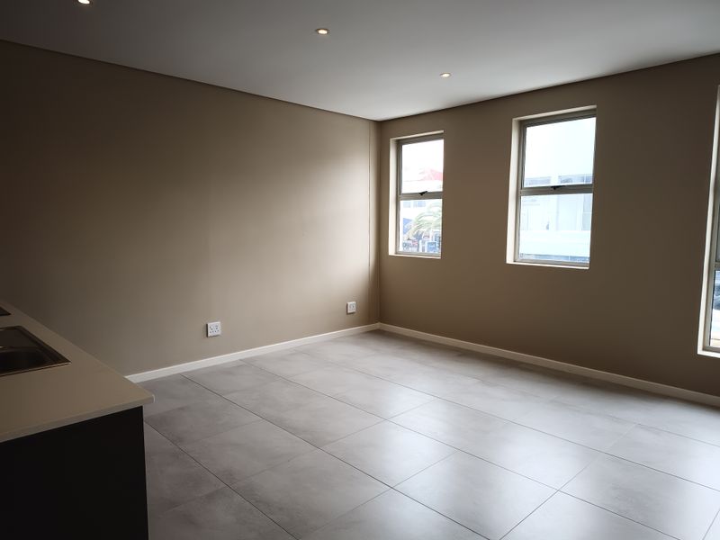 An empty open-plan living and kitchen area featuring modern tiled flooring, recessed downlights, and neutral wall tones.