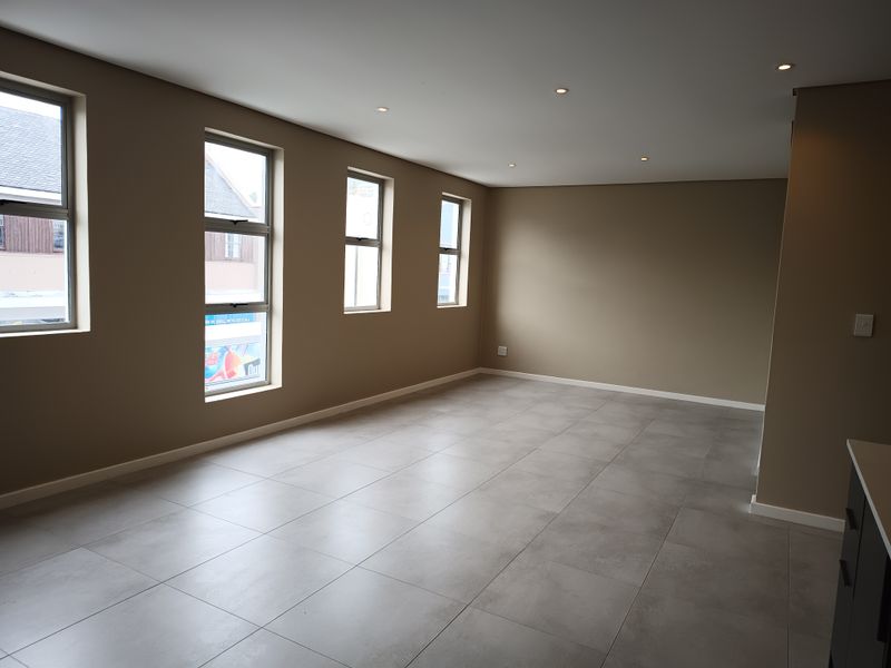 Spacious open-plan living area featuring modern large-format floor tiles, recessed downlighting, and multiple windows providing ample natural light.