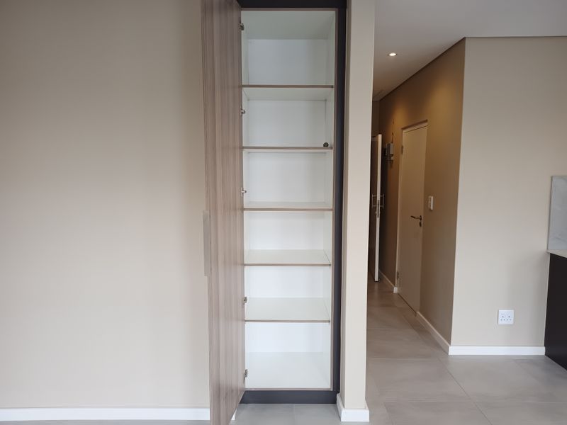 A clean, modern hallway featuring a built-in storage cupboard with wood-finish doors, neutral wall tones, and tiled flooring.
