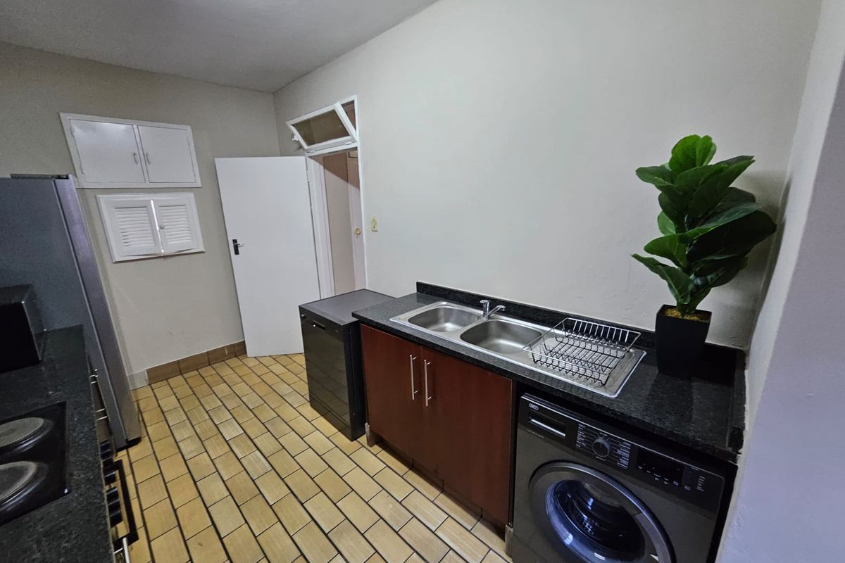 A functional kitchen area featuring granite countertops, a double basin sink, built-in cabinetry, and tiled flooring with space for under-counter appliances.
