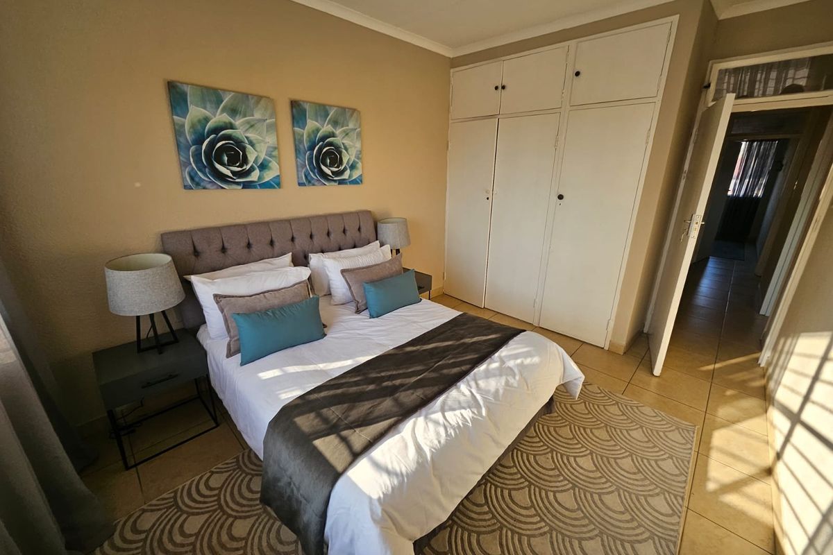 A well-lit bedroom featuring built-in cupboards and neutral tiled flooring, offering a comfortable and functional living space.