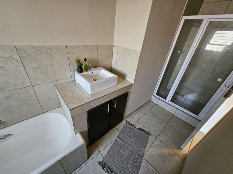 A functional bathroom featuring a built-in vanity with a vessel sink, a separate bathtub, and a glass-enclosed shower with neutral wall and floor tiling.