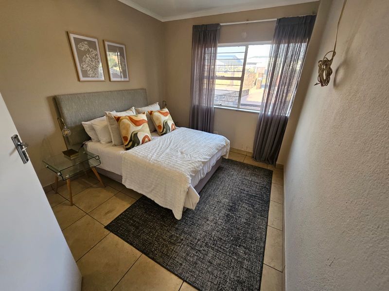 A functional bedroom featuring tiled flooring and a large window with curtain rails, providing natural light. Note the exposed electrical wiring on the wall.