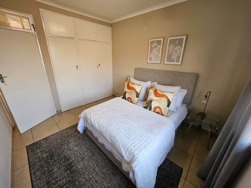 A well-maintained bedroom featuring neutral wall tones, tiled flooring, and ample built-in cupboard storage space.