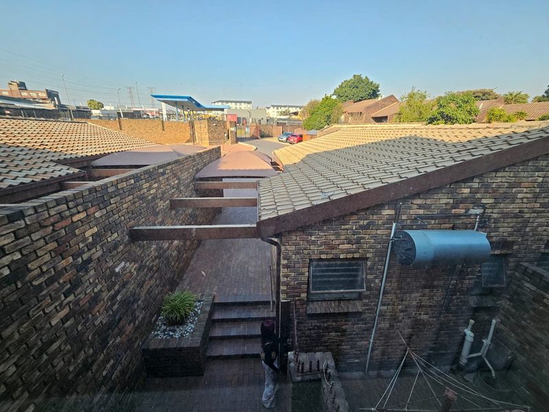 An elevated view of a rear courtyard area featuring brick construction, tiled roofing, paved pathways, and external utility fixtures.