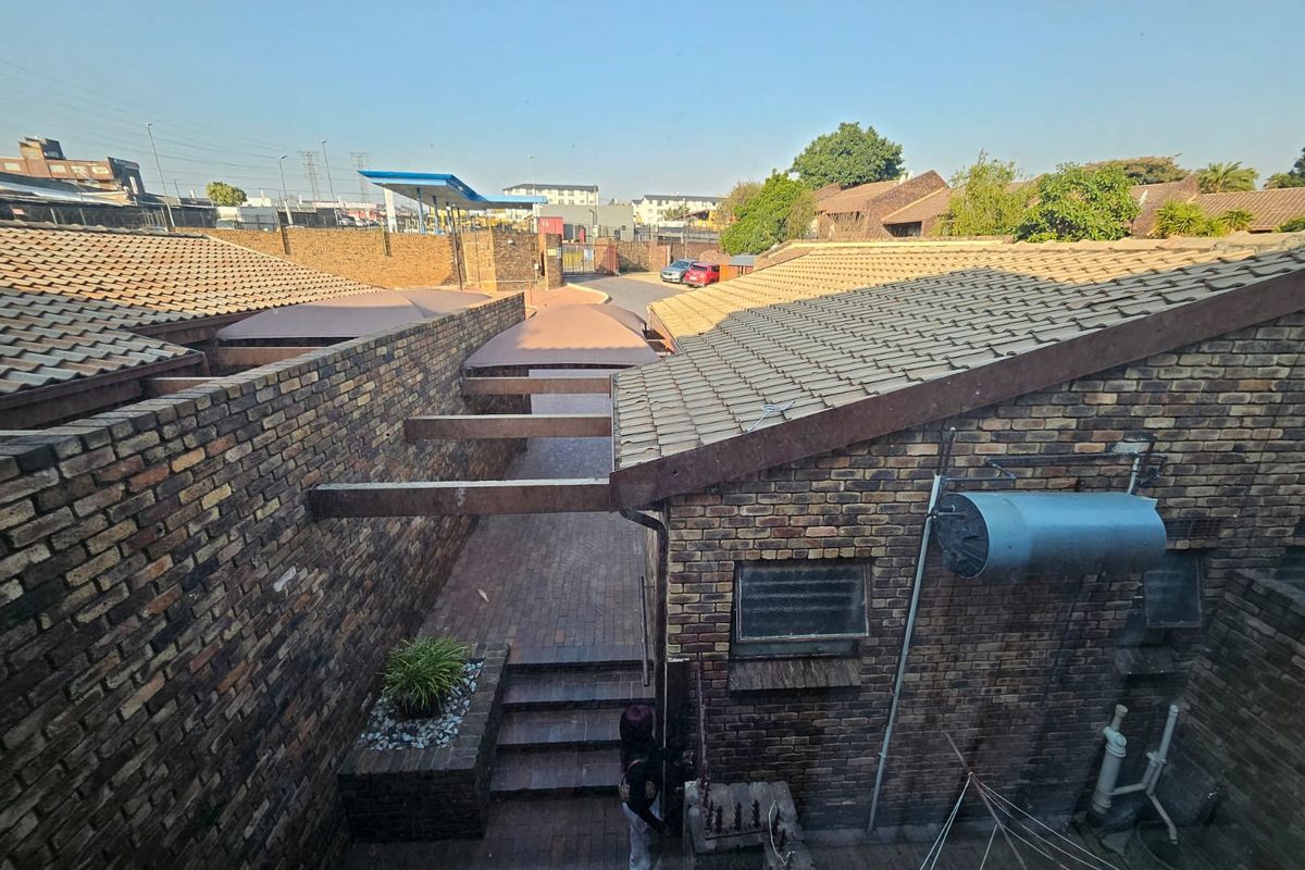 An elevated view of a rear courtyard area featuring brick construction, tiled roofing, paved pathways, and external utility fixtures.