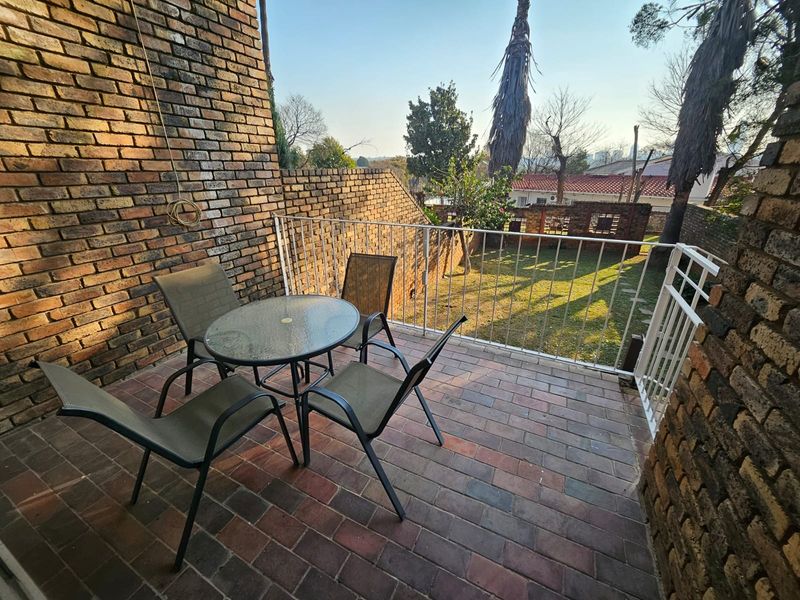 A private outdoor patio featuring brick paving, exposed brick walls, and a metal balustrade overlooking the garden area.