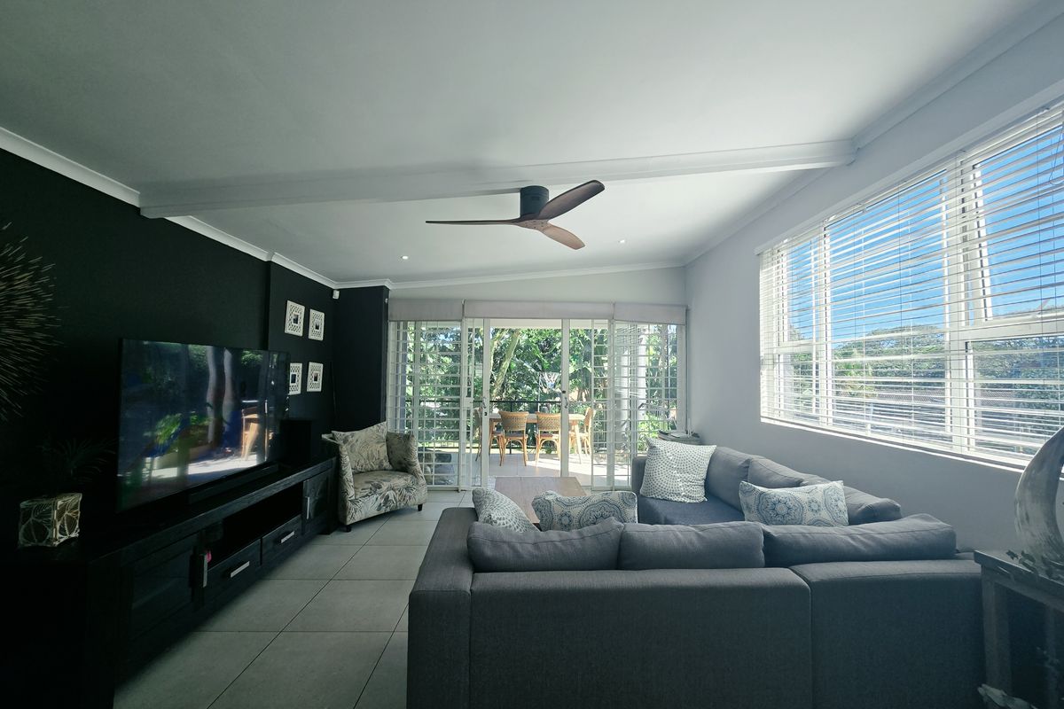 Spacious living room featuring tiled floors, a modern ceiling fan, and large sliding glass doors that provide natural light and access to the patio.