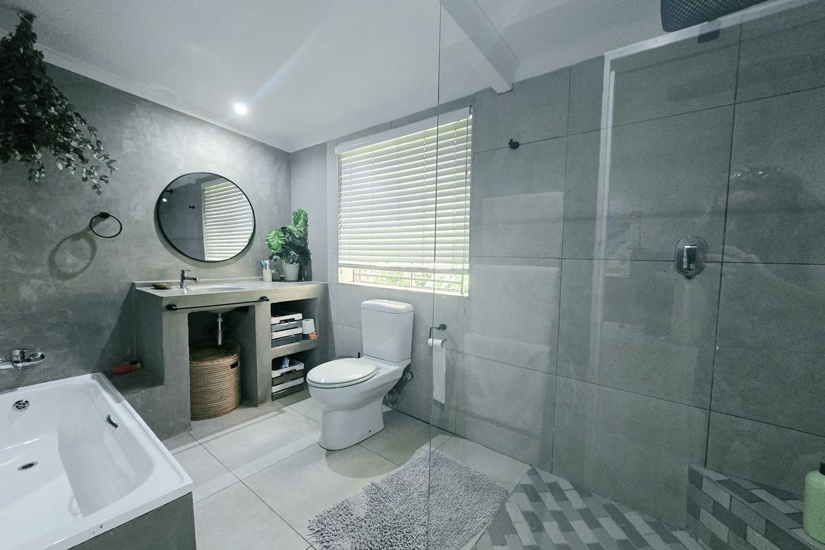 Modern bathroom featuring a built-in concrete vanity, walk-in shower with glass screen, separate bathtub, and contemporary grey tiling throughout.