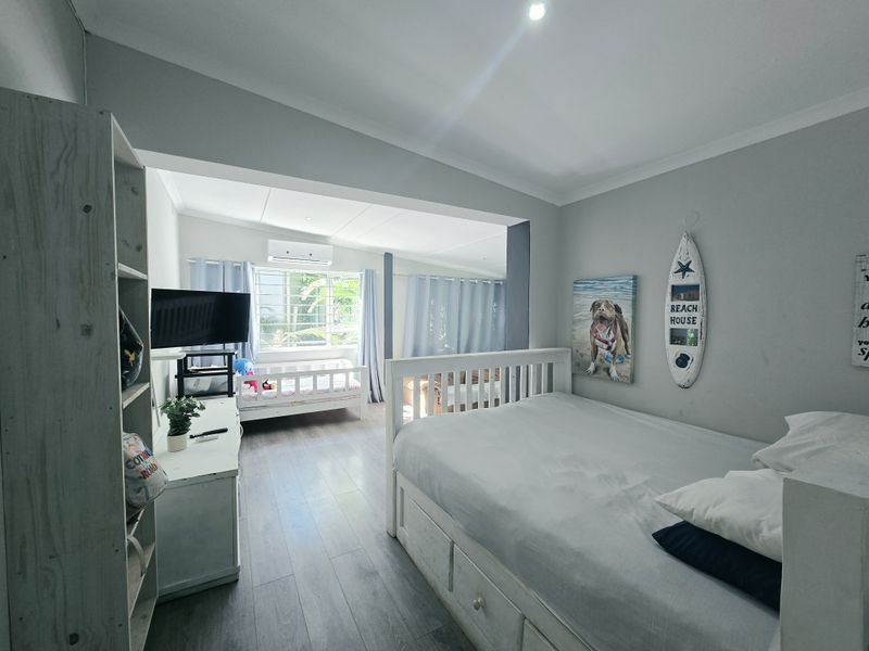 Spacious bedroom featuring laminate flooring, coved ceilings, recessed lighting, and a wall-mounted split-system air conditioner.