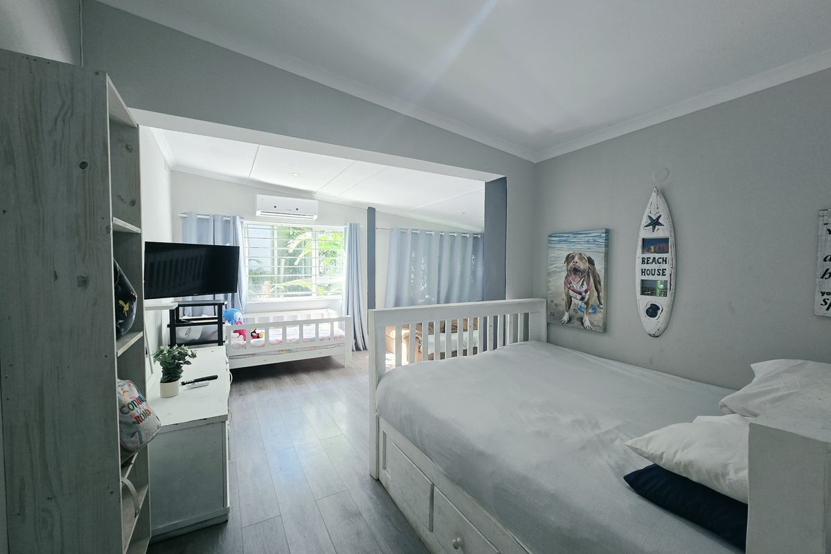 Spacious bedroom featuring laminate flooring, coved ceilings, recessed lighting, and a wall-mounted split-system air conditioner.