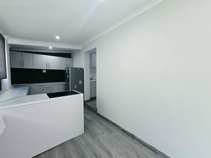 A functional kitchen featuring modern grey cabinetry, laminate flooring, and a built-in hob, with an adjacent scullery area visible.