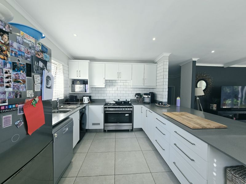 Modern open-plan kitchen featuring white cabinetry, stone countertops, subway tile backsplash, and stainless steel appliances, seamlessly flowing into the adjacent living area.