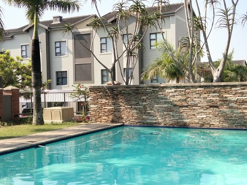 A well-maintained communal swimming pool area featuring a decorative stone cladding wall, paved surround, and landscaped garden setting within the apartment complex.