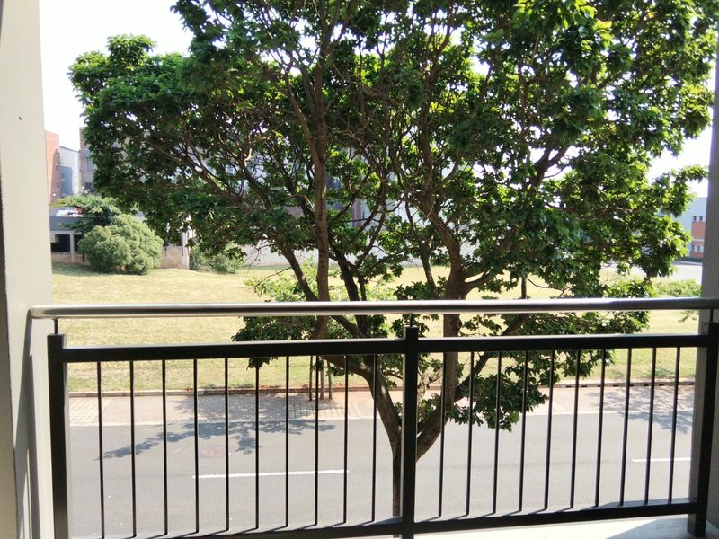 A private balcony featuring a modern metal balustrade with a stainless steel handrail, overlooking a street and mature tree.
