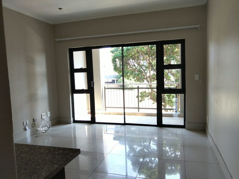 An empty open-plan living area featuring polished tiled floors, a granite breakfast counter, and large sliding doors leading to a private balcony.