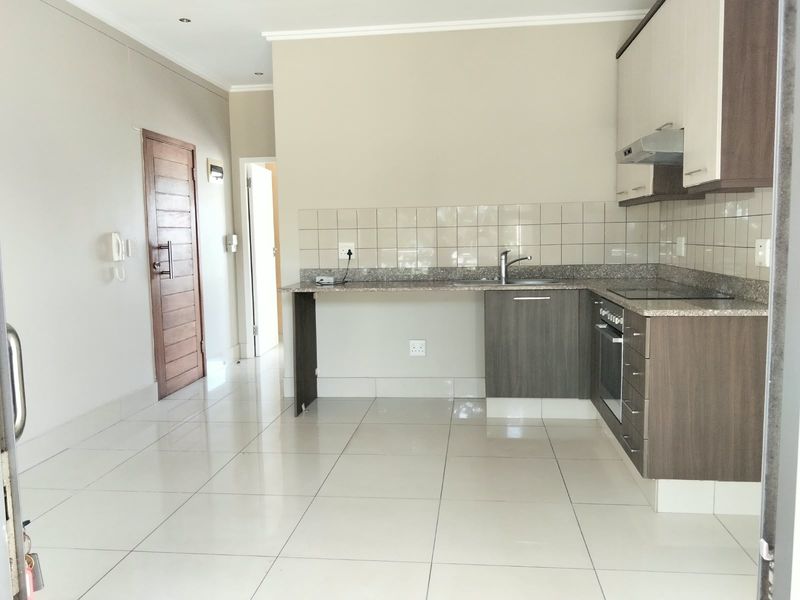 Modern open-plan kitchen featuring granite countertops, built-in oven, hob, extractor fan, and neutral tiled flooring in a clean, well-maintained apartment setting.