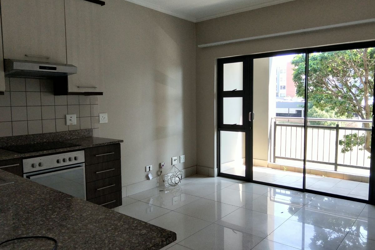 Open plan kitchen and living area featuring granite countertops, built-in oven, and large sliding doors leading to a private balcony with tiled flooring.