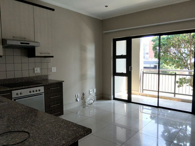 Open plan kitchen and living area featuring granite countertops, built-in oven, and large sliding doors leading to a private balcony with tiled flooring.