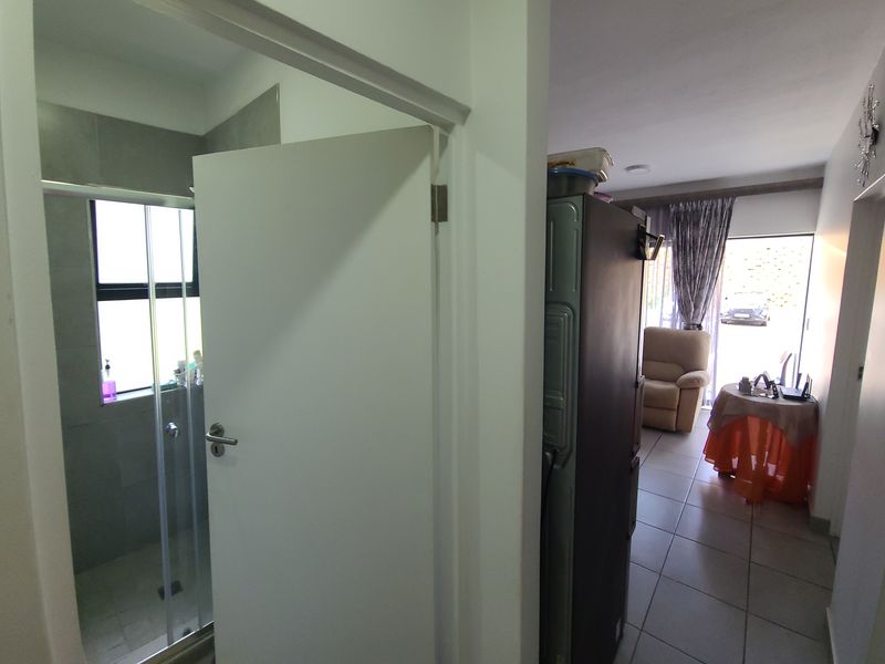 A view from a hallway looking into a bathroom with a shower enclosure and towards an open-plan living area with tiled flooring.