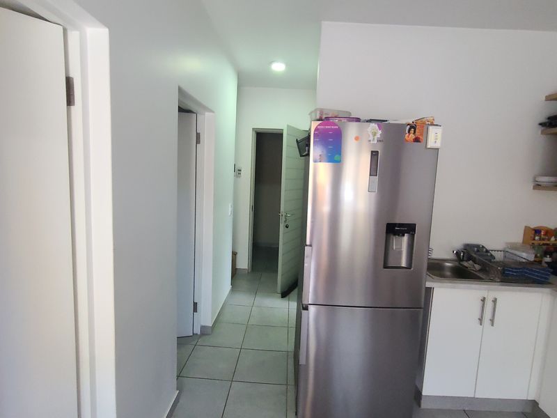 A functional kitchen area featuring tiled flooring, white cabinetry, and a stainless steel sink, leading into a hallway with access to other rooms.