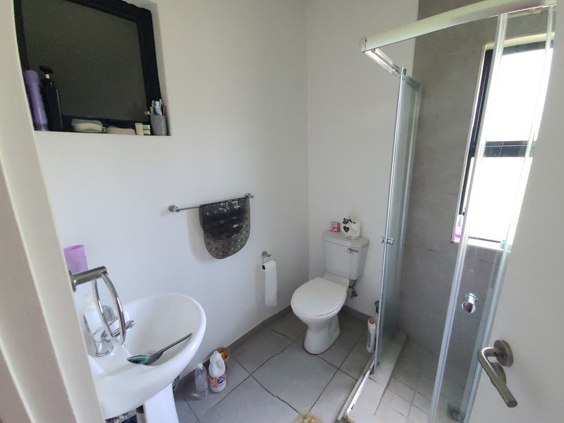 A functional bathroom featuring a pedestal basin, a standard toilet, and a glass-enclosed shower with tiled finishes.