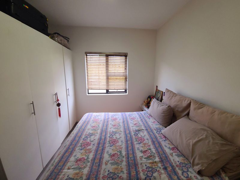 A functional bedroom featuring built-in cupboards and a window fitted with venetian blinds, offering a clean and simple living space.