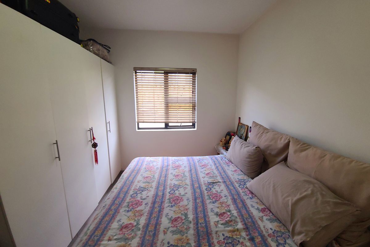 A functional bedroom featuring built-in cupboards and a window fitted with venetian blinds, offering a clean and simple living space.